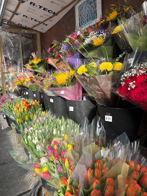 A display of freshly prepared floral bouquets arranged in large black containers at a flower shop. The arrangements include a variety of vibrant sunflowers, red roses, pink and orange tulips, white an